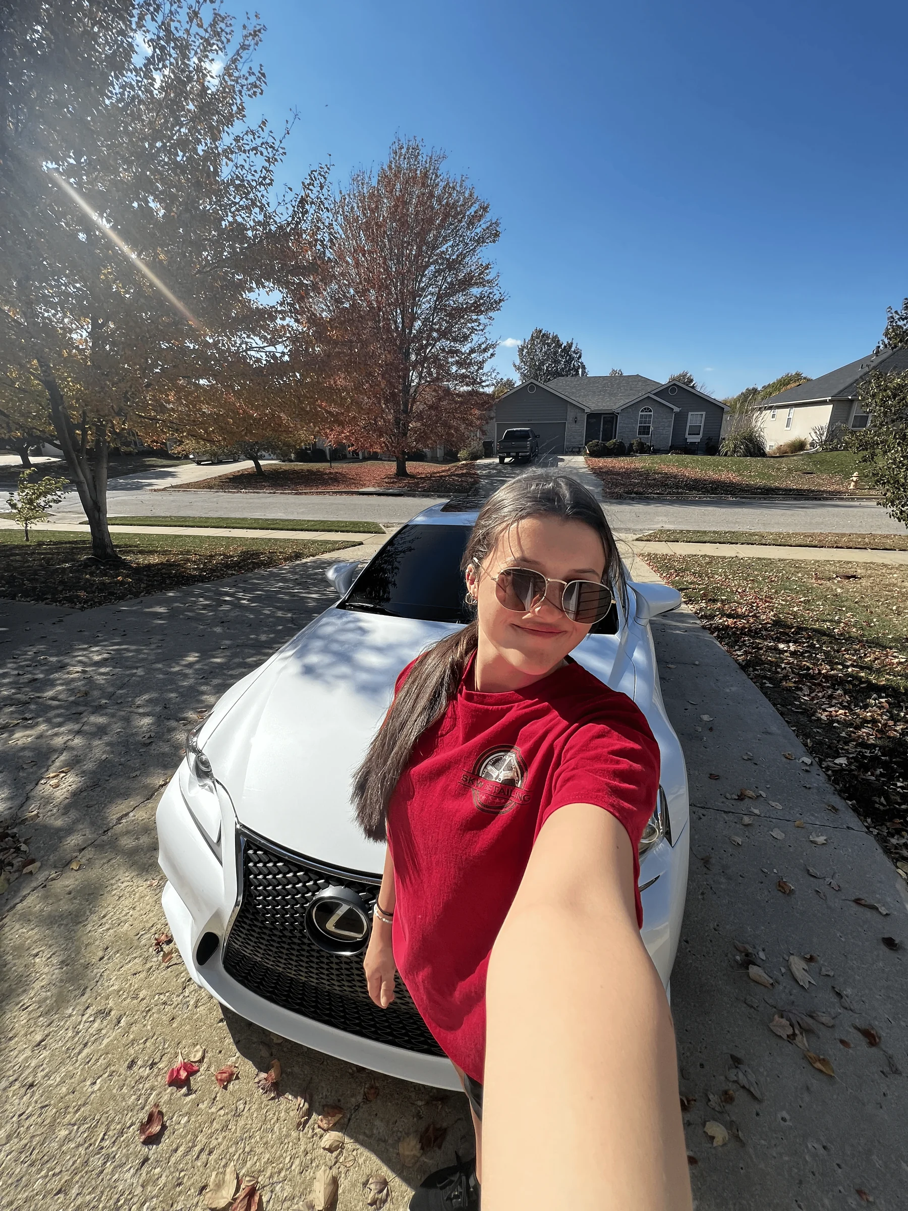 Shaleigh Walk, owner and detailer at SKW Detailing in Lawrence, KS, standing with a freshly detailed white Lexus in a sunny driveway